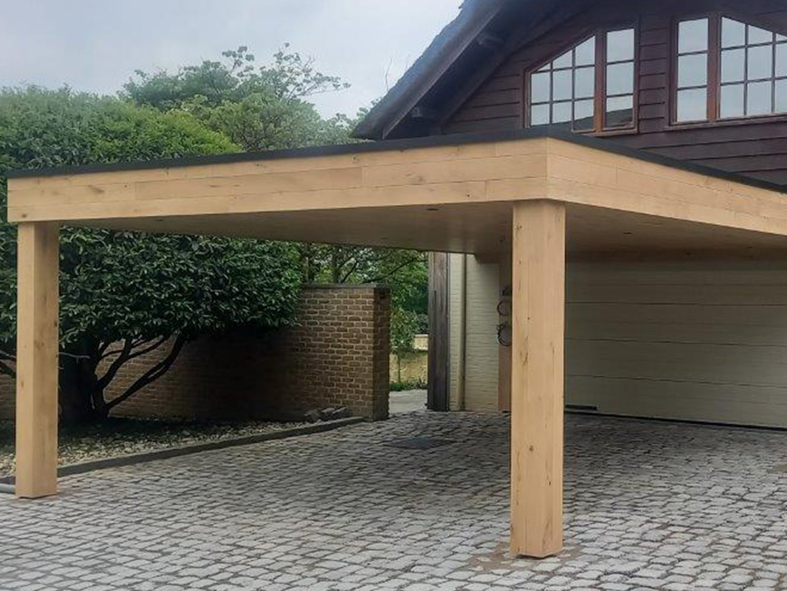 Carport met dak en kolommen in massief hout, op een kasseiende oprit naast een woning.