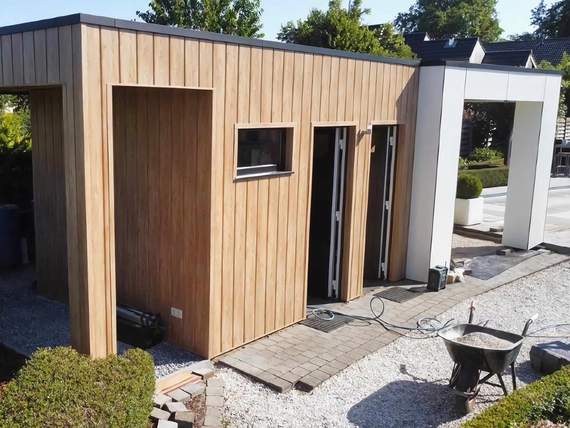 Poolhouse met verticale houten beplanking naast een zwembad, gefotografeerd tijdens de laatste werken.