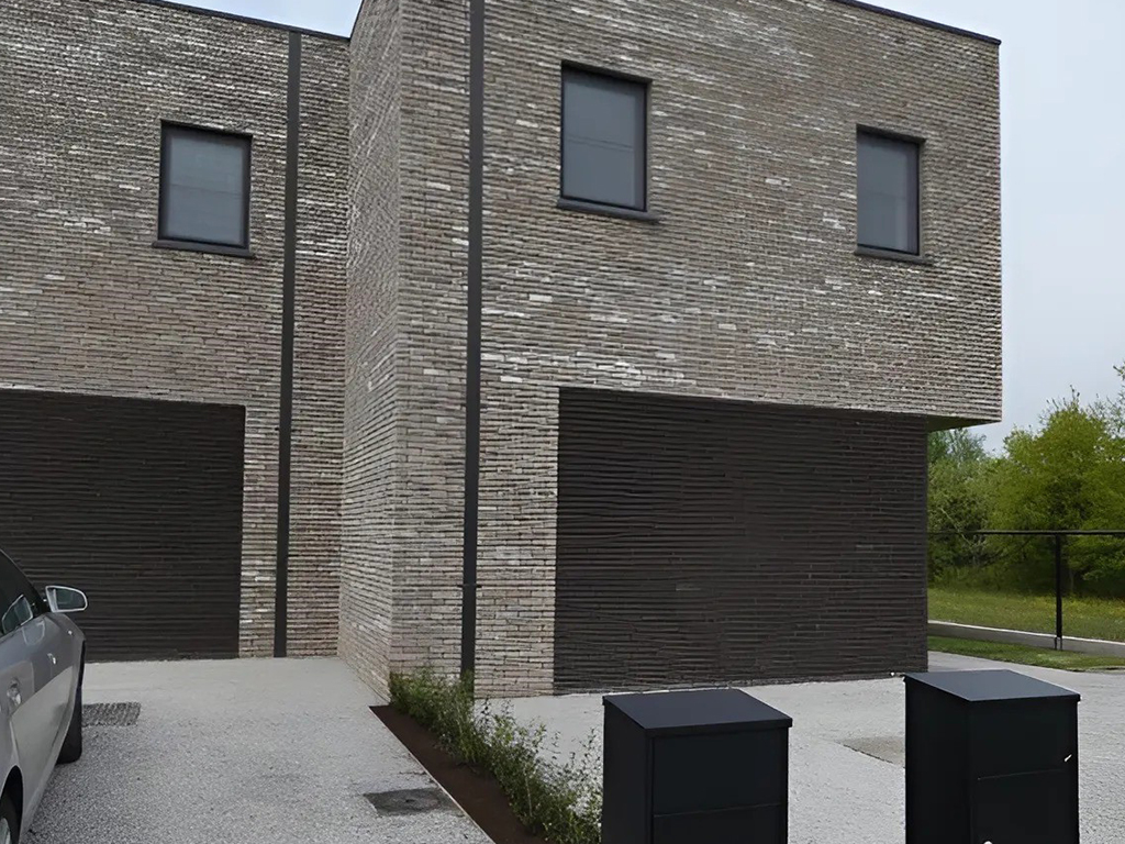 Twee afgewerkte halfopen woningen in lichte baksteen met donkere garagepoorten, gebouwd in houtskelet.